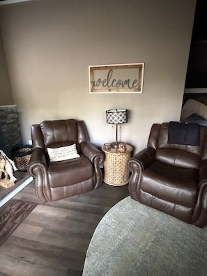 A living room with two leather armchairs, a round side table with a lamp, and a 'welcome' sign on the wall.