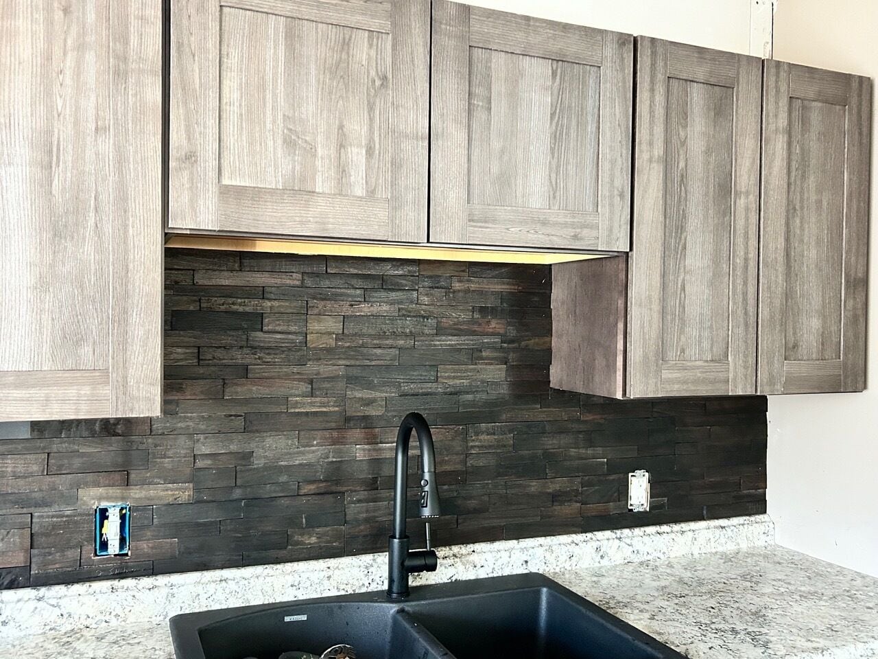 A kitchen with wooden cabinets, a black faucet, and a stone backsplash.