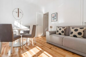 A modern living room with a grey sofa, a dining table with chairs, and a round wall clock. - 'Graça' Apartment with Private Terrace (Lisbon)