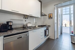 A modern kitchen with a dishwasher, stove, sink, and a view of the outside through a glass door. - 'Graça' Apartment with Private Terrace (Lisbon)