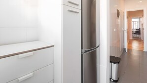 Cozinha moderna com armários brancos, geladeira de aço inoxidável e lixeira.