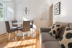 A modern living room with a grey sofa, a round dining table, and two chairs. - 'Graça' Apartment with Private Terrace (Lisbon)
