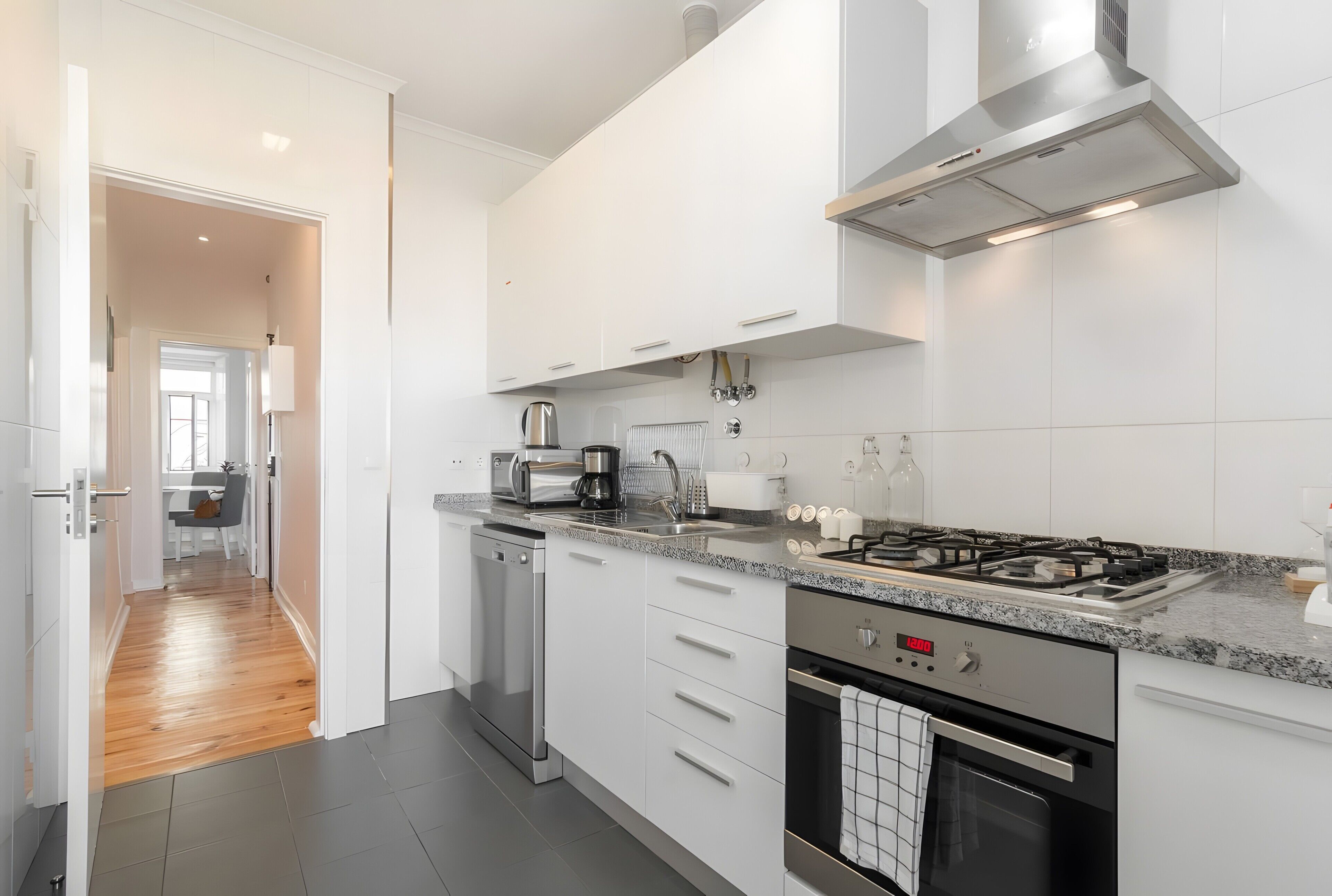 A modern kitchen with white cabinetry, a stainless steel range hood, a built-in dishwasher, and a gas stove.