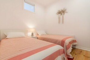 Ein Schlafzimmer mit zwei Betten, einem Nachttisch mit Lampe, Holzboden und einem Fenster.
