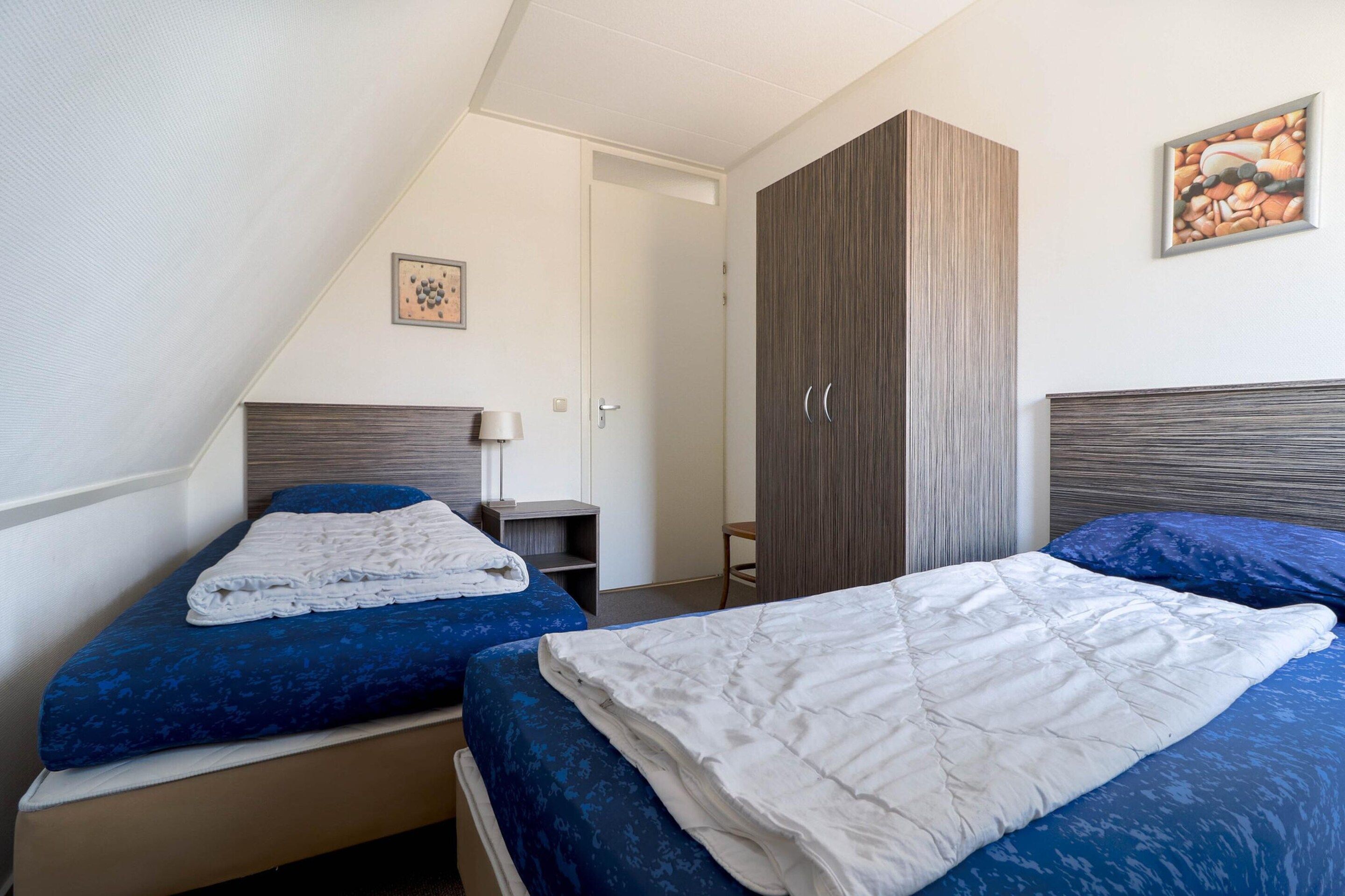 A bedroom with two beds, a wardrobe, a bedside table, and a painting on the wall.