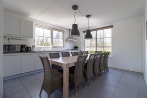 A modern kitchen with white cabinets, a dining table with wicker chairs, and pendant lights. - Family Beach Villa With Outdoor Spa (Makkum)