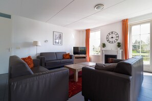 A modern living room with a sofa, armchairs, a TV, and a fireplace. - Family Beach Villa With Outdoor Spa (Makkum)