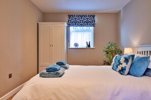 A bedroom with a bed, a window with a patterned valance, a door, a bedside plant, and a lamp. - Romantic Retreat in Lincolnshire (Sleaford)