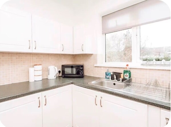 A kitchen with white cabinets, a microwave, a sink, and a window.