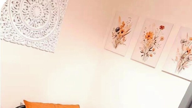 Uma cama de solteiro com roupa de cama laranja, uma mesa de cabeceira de madeira e um objeto decorativo na parede.