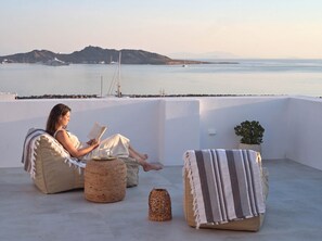 Eine Person entspannt auf einem Balkon mit Blick auf das Meer und Boote.