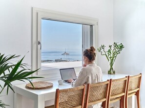 Una persona seduta a una scrivania bianca con un laptop, rivolta verso una grande finestra che si affaccia su un porto turistico con barche.