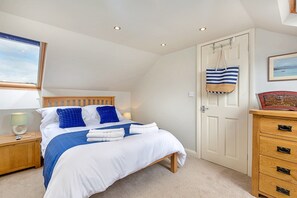 A bedroom with a bed, a nightstand, a dresser, a door, and a window with a view. - Beach House With Sea Views (Filey)
