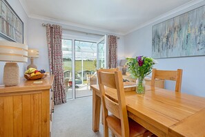 A dining area with a wooden table, chairs, a vase of flowers, and a fruit bowl on a wooden cabinet. - Beach House With Sea Views (Filey)