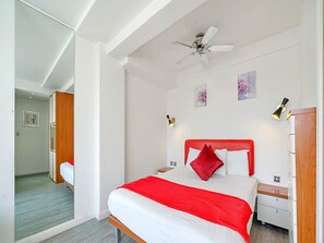 A hotel room with a bed, bedside tables, a wardrobe, a ceiling fan, and artwork on the wall. - Kensington Stay With Bath (London)