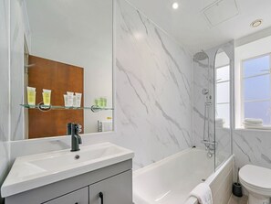 A bathroom with a white sink, a mirror, a shower, and a toilet. - Kensington Stay With Bath (London)
