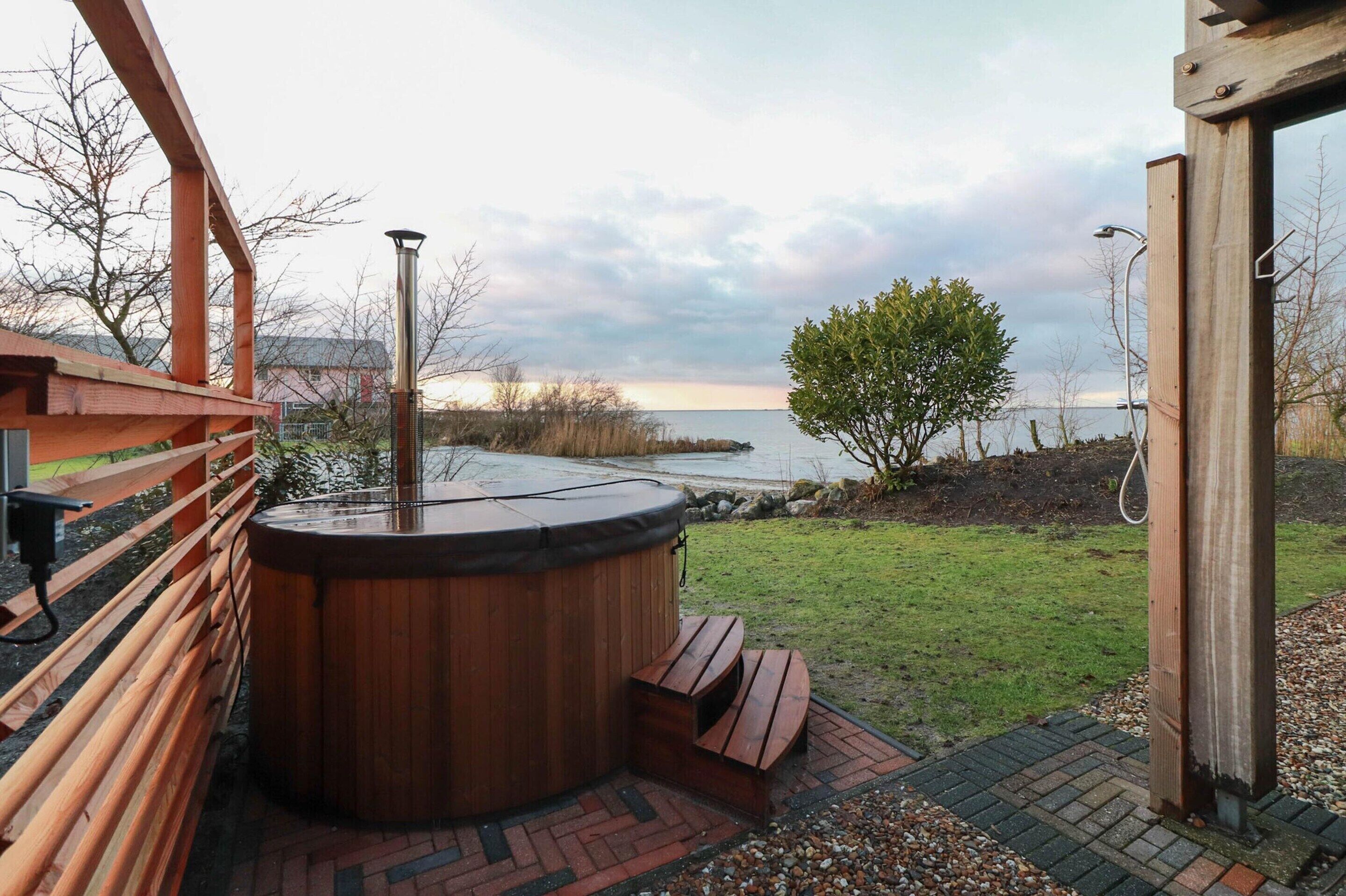 A wooden deck with a hot tub, a wooden fence, and a view of a body of water.