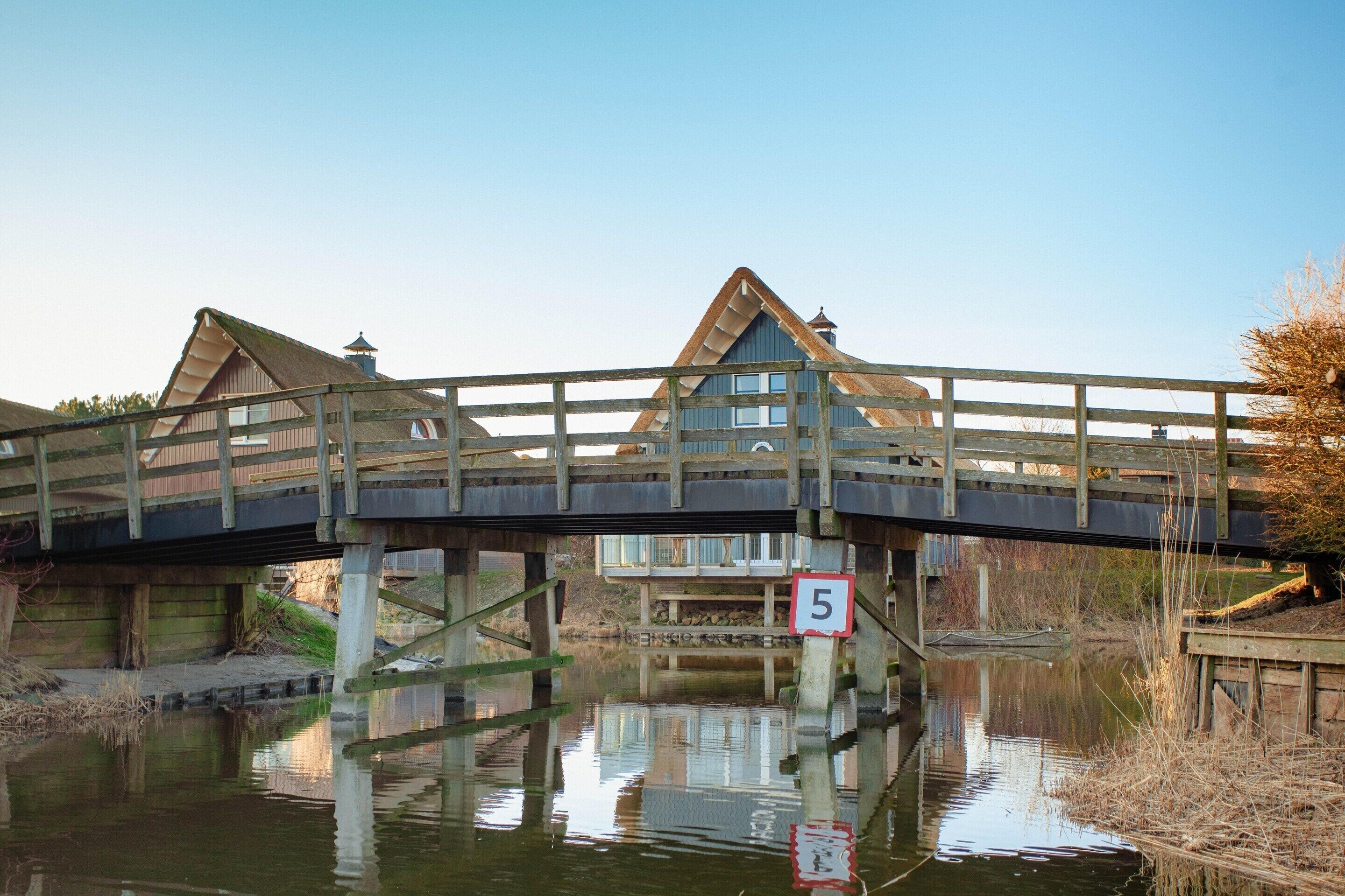Een houten brug met een snelheidsbeperking van 5, over een waterlichaam met gebouwen aan weerszijden.