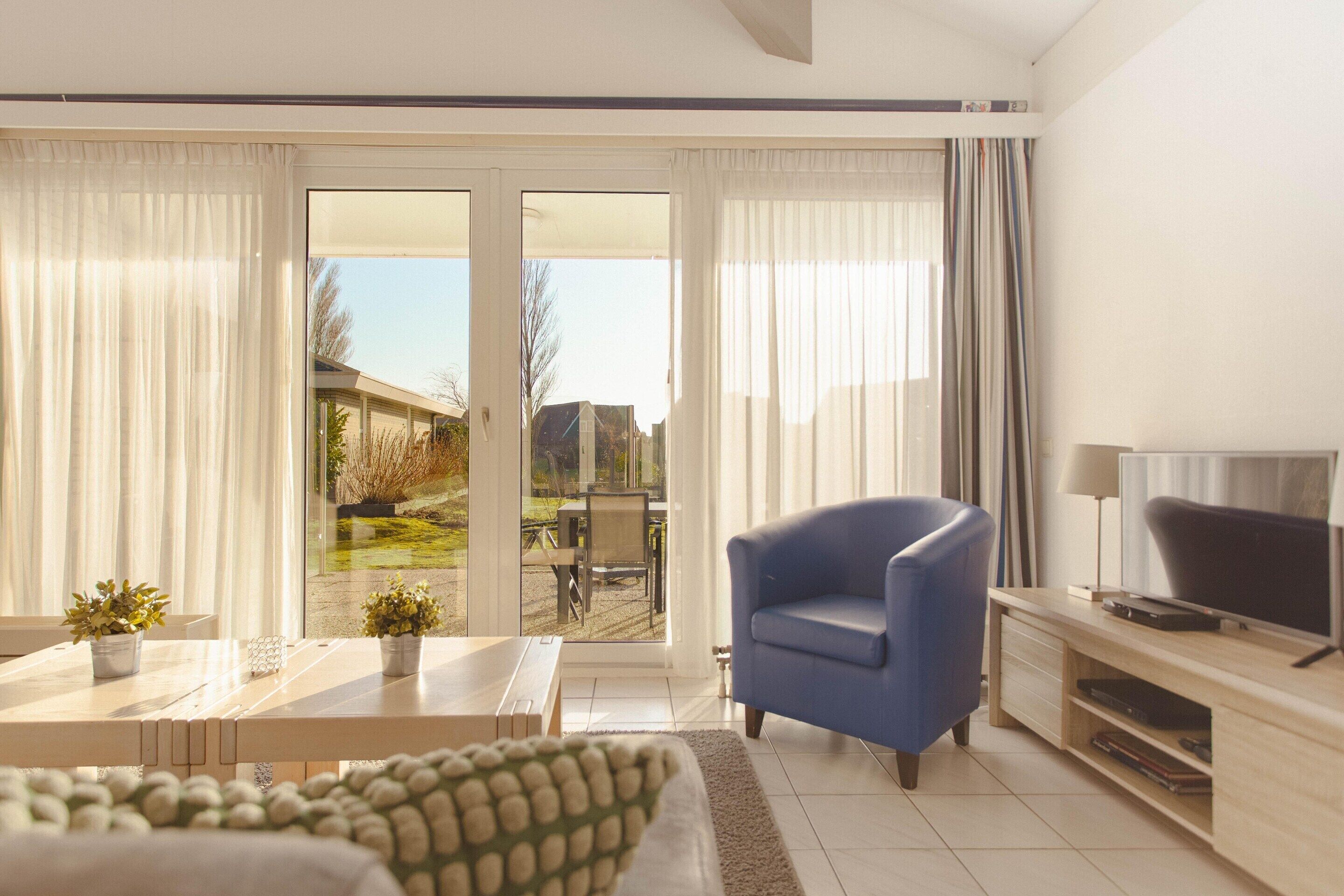 Una sala moderna con un sofá, un sillón azul, un televisor y un comedor con una mesa y sillas.