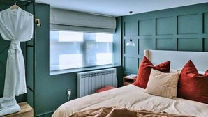 A bedroom with a bed, a window, a radiator, and a hanging robe. - Weald Base for Four Guests (Tenterden)