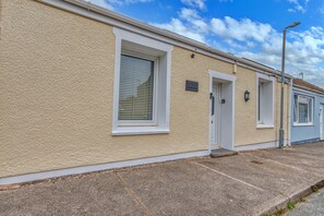 A row of single-story buildings with a textured facade, white-framed windows, and a street lamp. - Romantic Devon Cottage for 2 (Pembroke Dock)