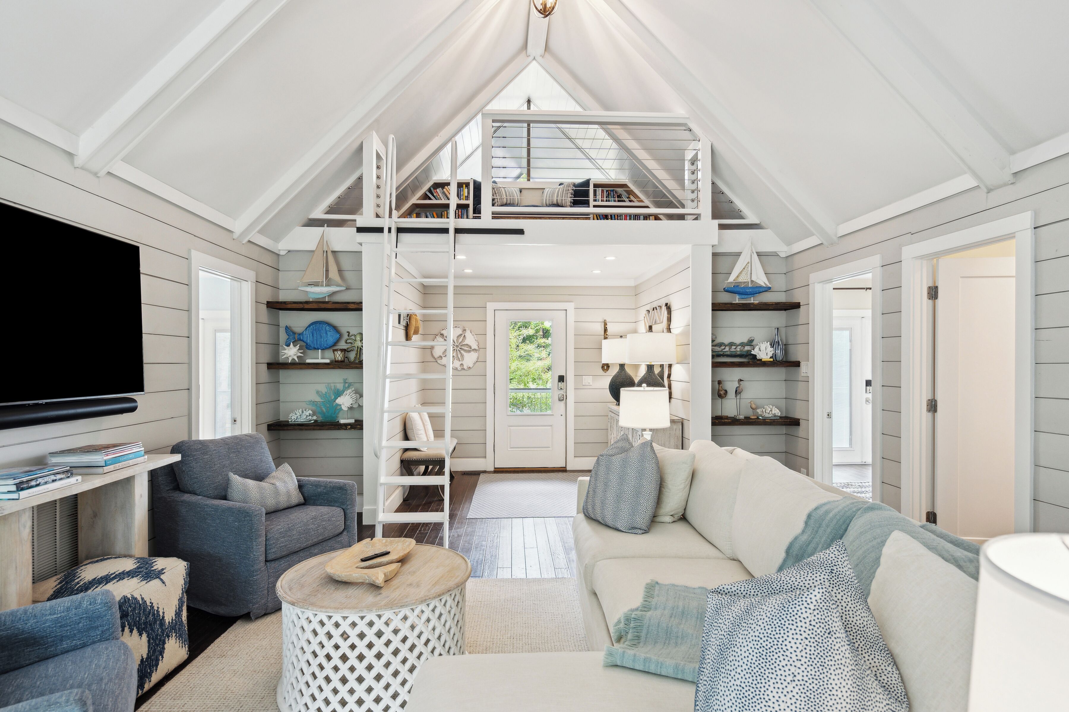 A spacious living room with a high ceiling, a television, a sofa, a coffee table, and a bookshelf.
