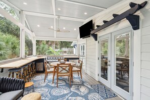 Un espace cuisine extérieur abrité, équipé d’un ensemble de mobilier de salle à manger et de tabourets de bar.