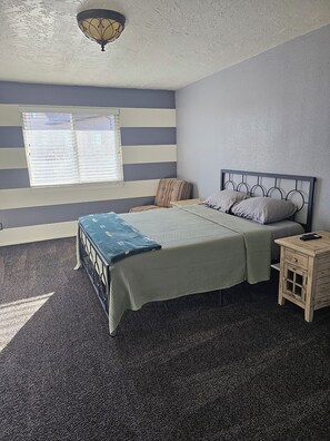 A bedroom with a bed, bedside table, and a window with blinds.