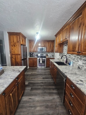 A kitchen with wooden cabinets, granite countertops, stainless steel appliances, and a tiled backsplash.
