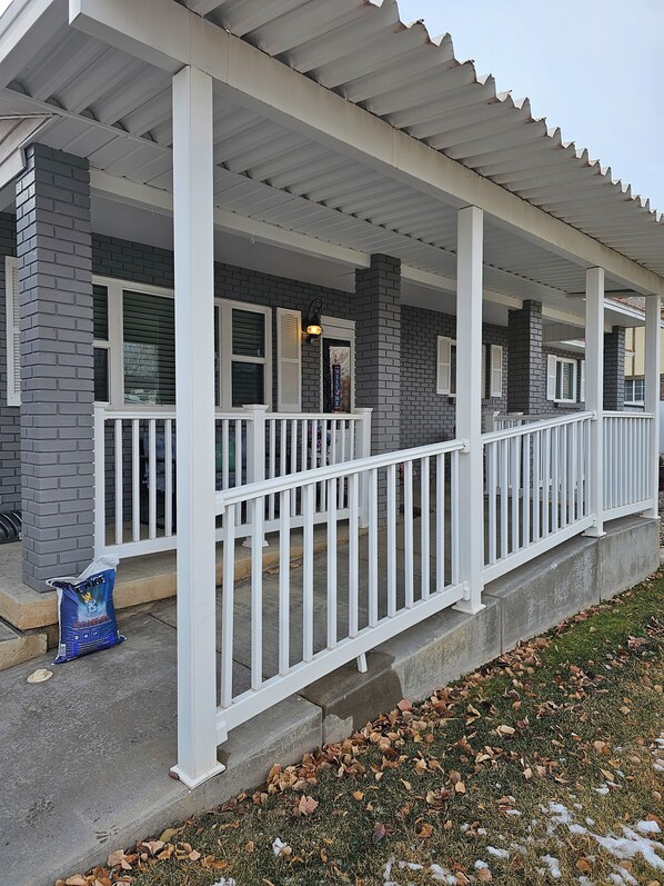 A covered porch with white railings and a brick exterior.