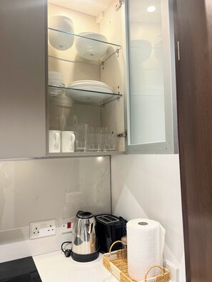 Eine Küche mit einer Glasablage, auf der Teller, Gläser, ein Wasserkocher, ein Toaster und ein Korb stehen.