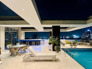 Área de piscina no terraço com vista para a cidade, móveis modernos e um bar.
