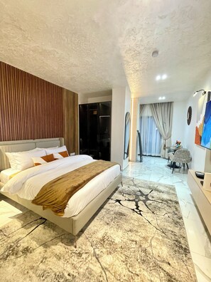 Ein modernes Hotelzimmer mit einem großen Bett, einem Boden mit Marmoroptik, einer Wandpaneele aus Holz, einem Fernseher und einer Sitzecke mit Tisch und Stühlen.