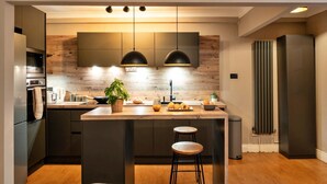 A modern kitchen with a central island, pendant lighting, and a built-in oven. - Elegant Apartment in Regency Cheltenham (Cheltenham)