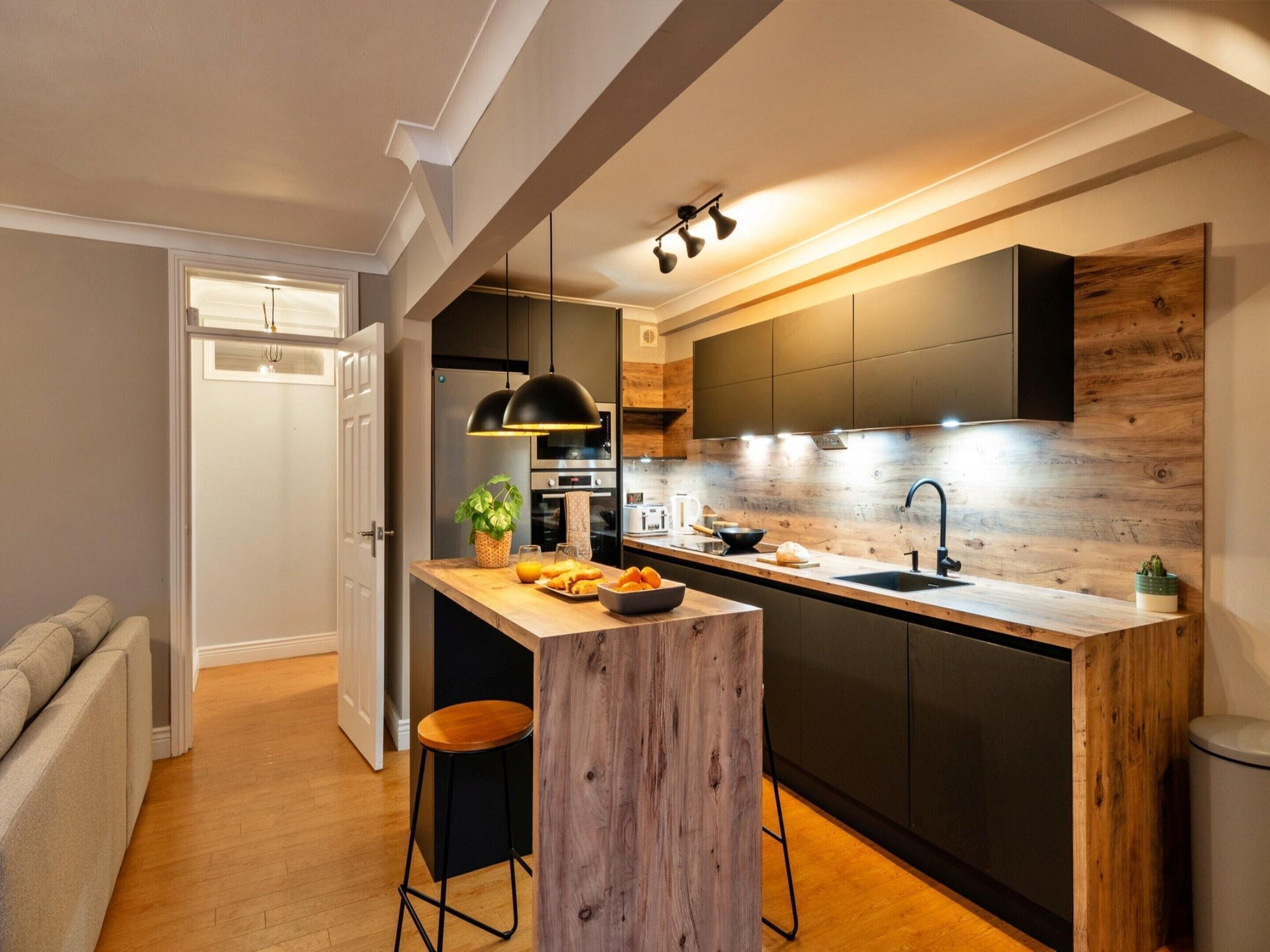 A modern kitchen with a wooden island, black cabinets, and a built-in oven.