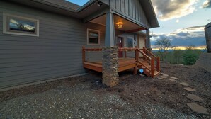 A residential building with a stone staircase leading to a wooden deck, a covered porch, and a view of the surrounding landscape. - Sunset Views (Blairsville)
