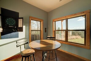 A room with a dartboard, a table with chairs, and large windows with a view of trees and sky. - Sunset Views (Blairsville)