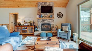 A cozy living room with a stone fireplace, a mounted television, and comfortable seating. - Sunset Views (Blairsville)