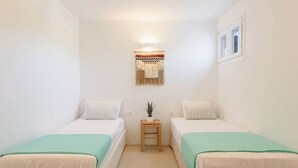 A small, clean room with two single beds, a small table with a plant, and a wall-mounted light fixture. - Owl’s Nest · Tsoukalia · Walk to Beach (Τοπική Κοινότητα Αρχιλόχου)