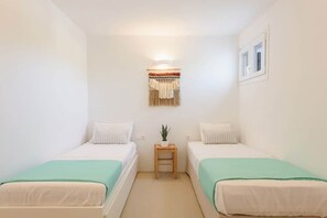A small, clean room with two single beds, a small table with a plant, and a wall-mounted light fixture. - Owl’s Nest · Tsoukalia · Walk to Beach (Τοπική Κοινότητα Αρχιλόχου)