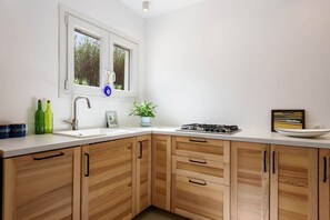 A kitchen with a white countertop, wooden cabinets, a window with a view, a sink, and a stove. - Owl’s Nest · Tsoukalia · Walk to Beach (Τοπική Κοινότητα Αρχιλόχου)