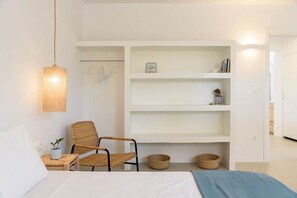 A bedroom with a bed, a chair, a shelf unit, and a hanging light fixture. - Owl’s Nest · Tsoukalia · Walk to Beach (Τοπική Κοινότητα Αρχιλόχου)
