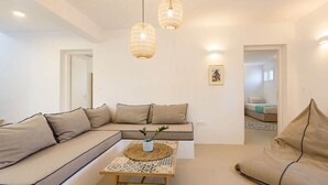 A modern living room with a sectional sofa, a coffee table with a woven top, and two hanging light fixtures. - Owl’s Nest · Tsoukalia · Walk to Beach (Τοπική Κοινότητα Αρχιλόχου)