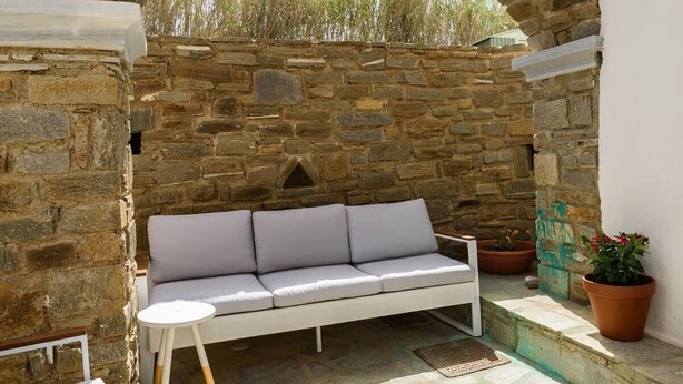 A stone-walled outdoor seating area with a white sofa and a small round table. - Owl’s Nest · Tsoukalia · Walk to Beach (Τοπική Κοινότητα Αρχιλόχου)