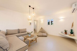 Ein modernes Wohnzimmer mit einer Couch, einem Couchtisch und einem Sitzsack. Ein Fenster bietet einen Ausblick, und ein Regal beherbergt Pflanzen.