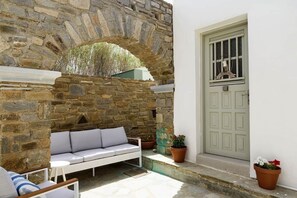 A stone archway, a white door, and a white sofa with cushions. - Owl’s Nest · Tsoukalia · Walk to Beach (Τοπική Κοινότητα Αρχιλόχου)