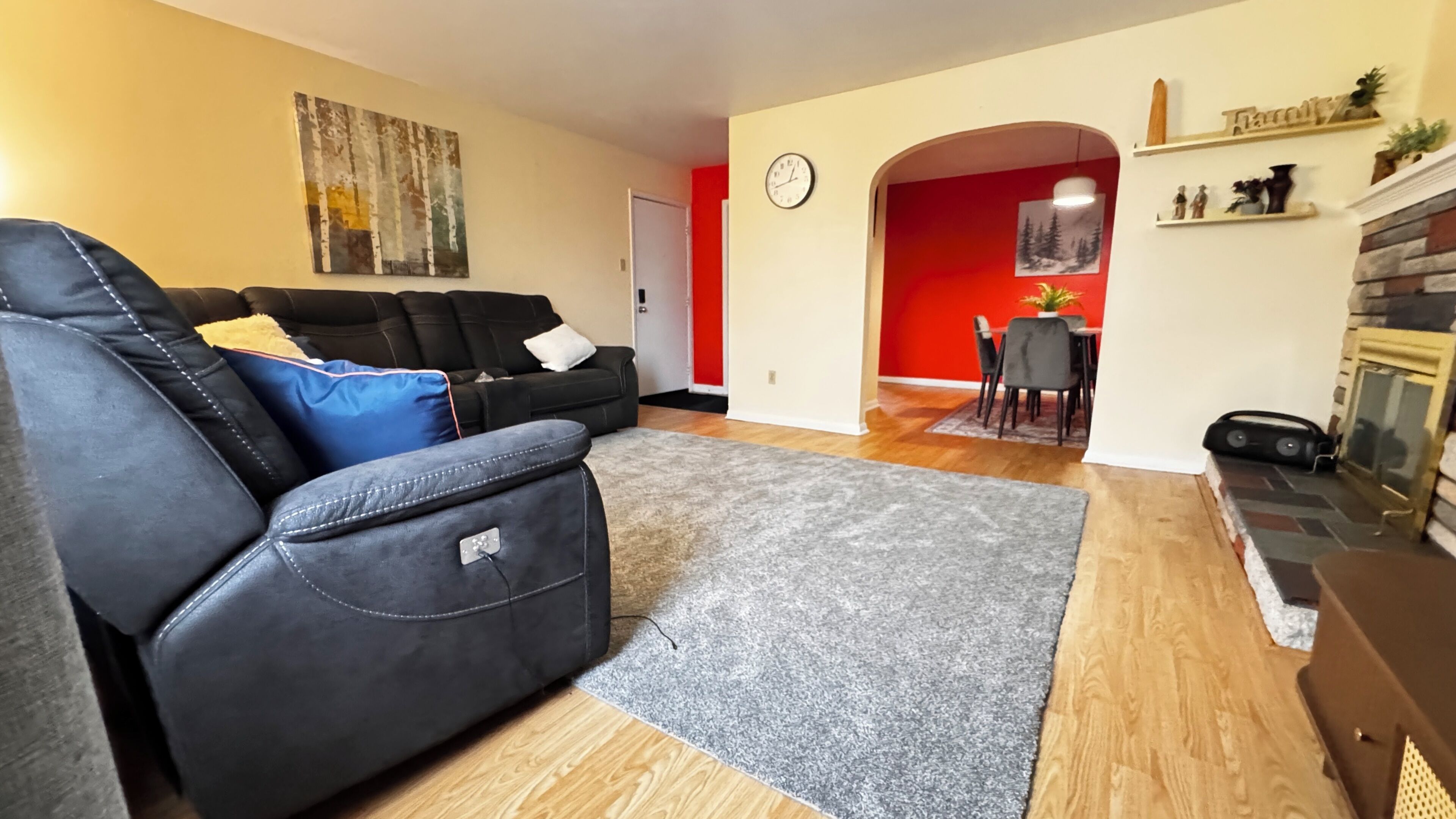 Sala de estar con sofá negro, alfombra gris, chimenea y comedor con pared roja.