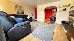 A living room with a black sofa, a grey rug, a fireplace, and a dining area with a red wall. - Summit Nest
A spacious cozy apartment for your comfort and relaxation (Saint John)
