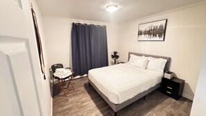 A hotel room with a bed, bedside table, chair, and a window with curtains.