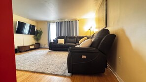 A living room with a sofa, a recliner, a flat-screen TV, a plant, and a lamp.